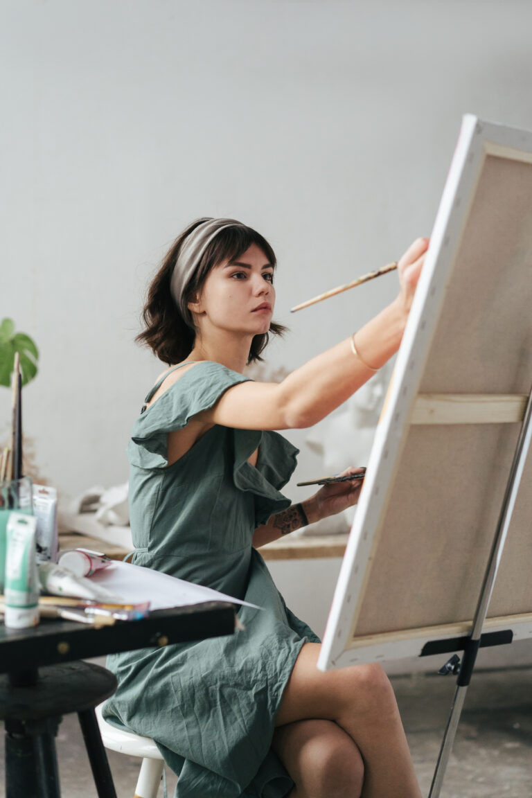 young woman painting canvas while sitting table